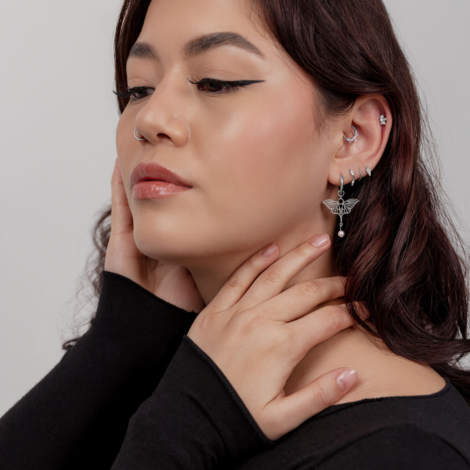 Donna con diversi orecchini, tra cui un orecchino a libellula con perla, su sfondo chiaro