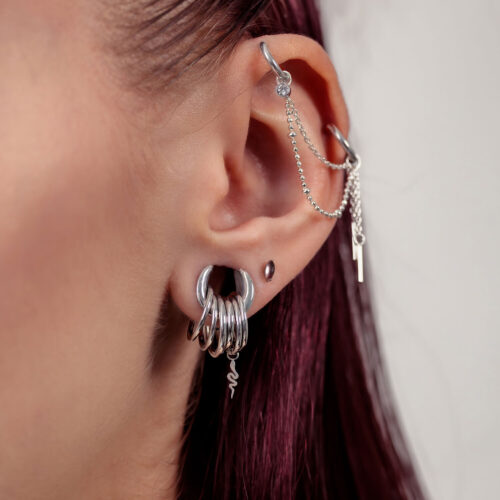 Primo piano di un orecchio con catena piercing d'argento e diversi anelli d'argento