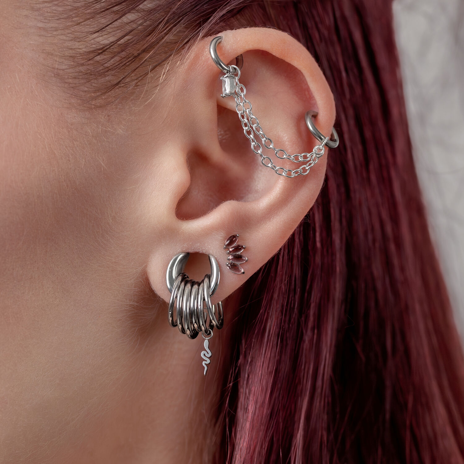 Orecchio con diversi piercing in argento e una catena su sfondo bianco