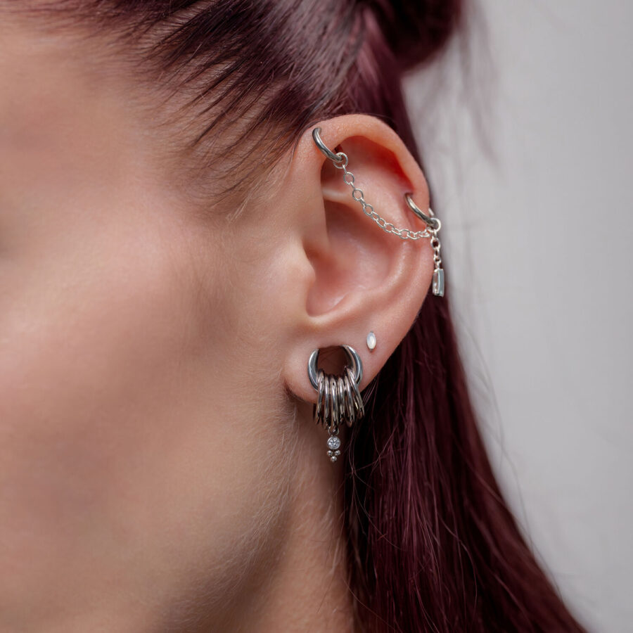 Orecchio con catena piercing in argento e diversi piercing, vista laterale