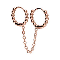 Due huggie piercing in oro rosa con sfere collegate e catena su sfondo bianco