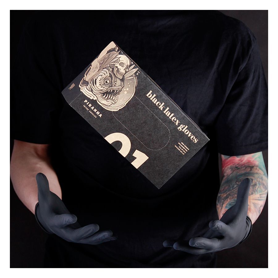 Persona con maglietta nera tiene una scatola di guanti in lattice Piranha neri su sfondo scuro