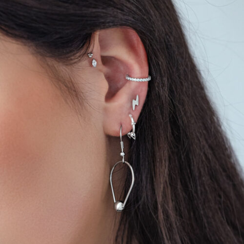 Primo piano di un orecchio con diversi piercing in argento, incluso un attacco di cristallo