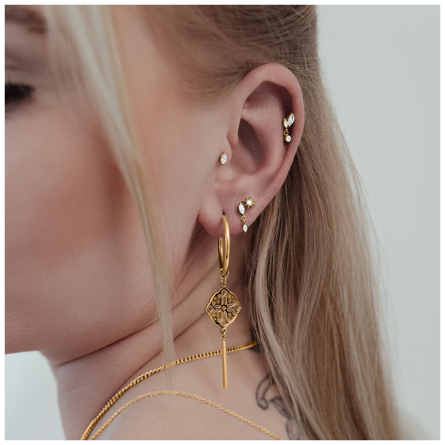 Labret Push Fit Cristallo Stella Oro 9,0 mm Primo piano di un orecchio con diversi piercing dorati, incluso un Labret Push Fit Cristallo Stella di 9,0 mm di lunghezza.