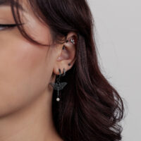 Primo piano di un orecchio con diversi piercing neri, incluso un attacco a forma di loto con un piccolo pendente.