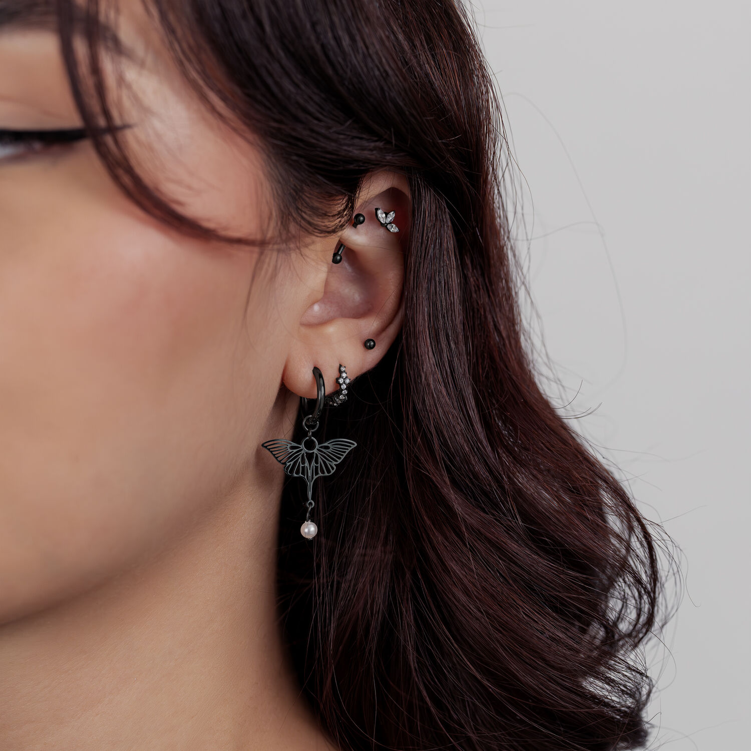 Primo piano di un orecchio con diversi piercing neri, incluso un attacco a forma di loto con un piccolo pendente.