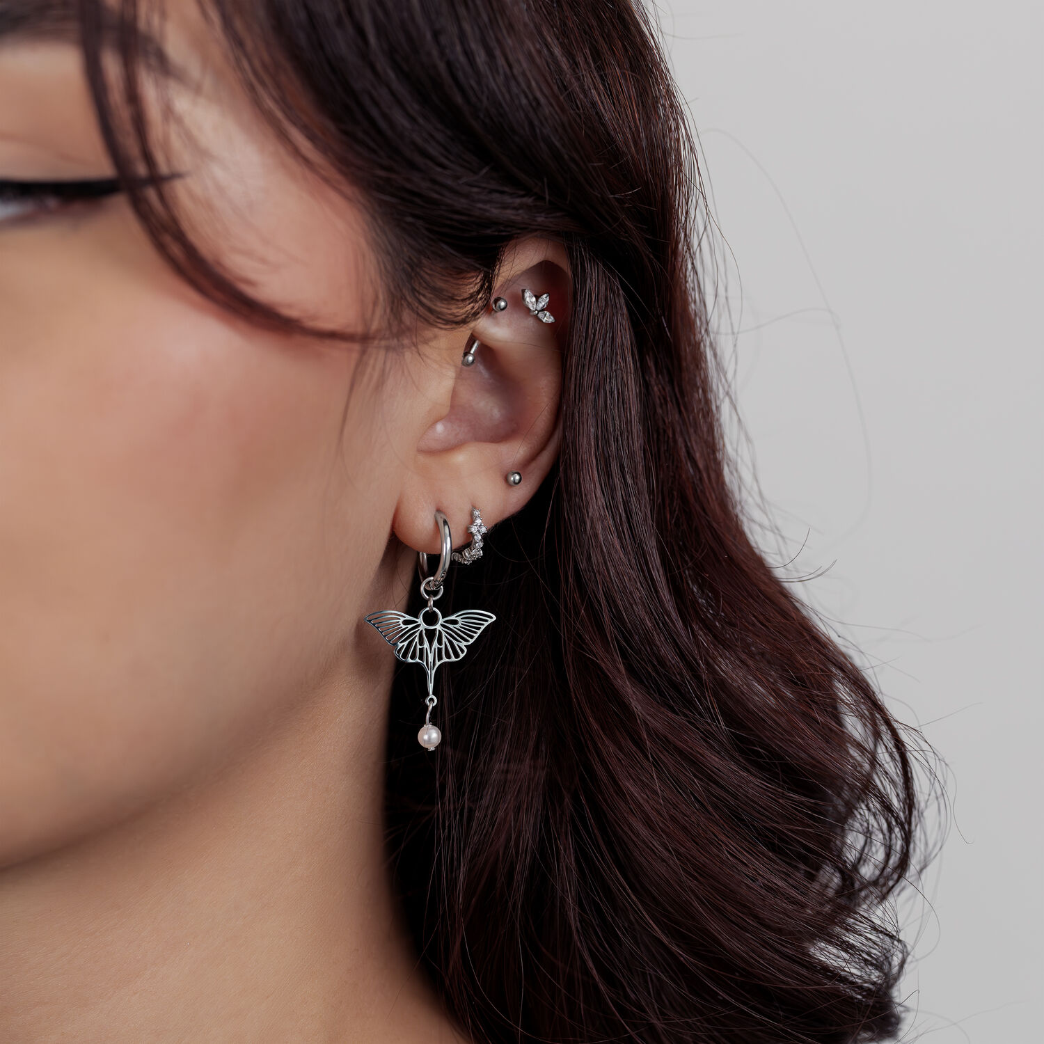 Donna con diversi piercing all'orecchio in argento e un ciondolo a farfalla su sfondo chiaro