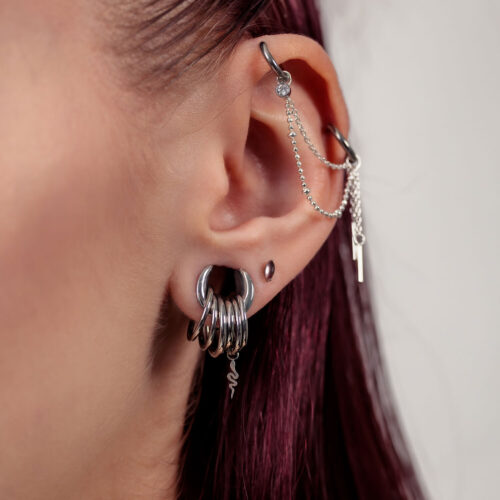 Primo piano di un orecchio con inserti piercing in argento e catene