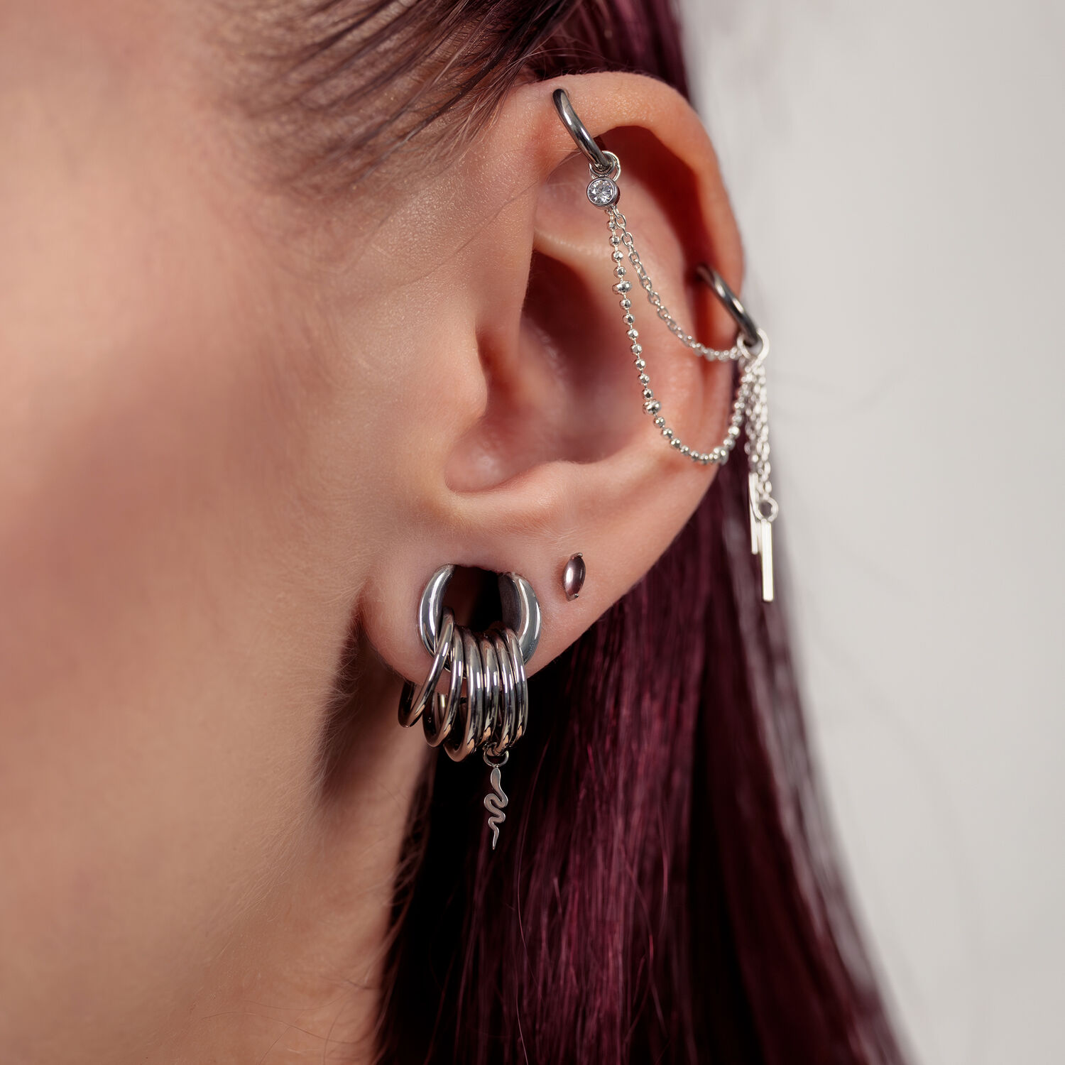 Primo piano di un orecchio con inserti piercing in argento e catene