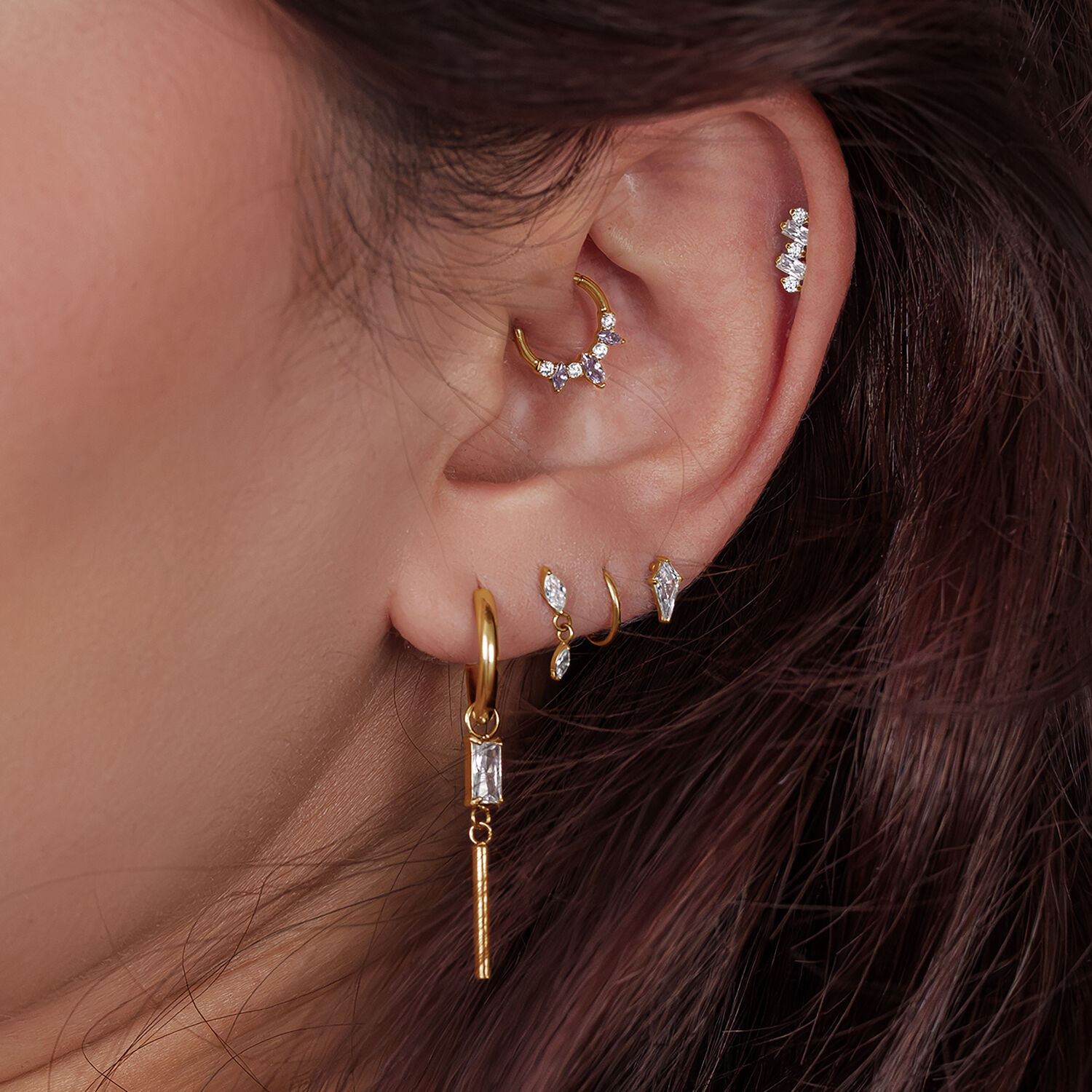 Primo piano di un orecchio con diversi piercing in oro e cristalli in varie posizioni