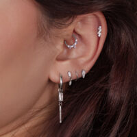 Primo piano di un orecchio con diversi piercing in argento, alcuni decorati con cristalli