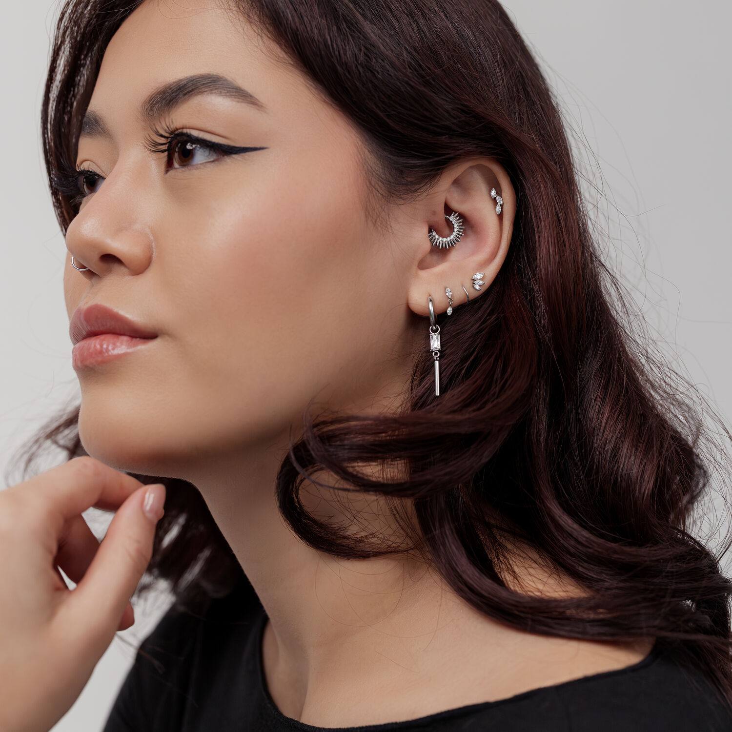 Donna con diversi piercing in argento a orecchio e naso, clicker per setto a forma di raggi di sole