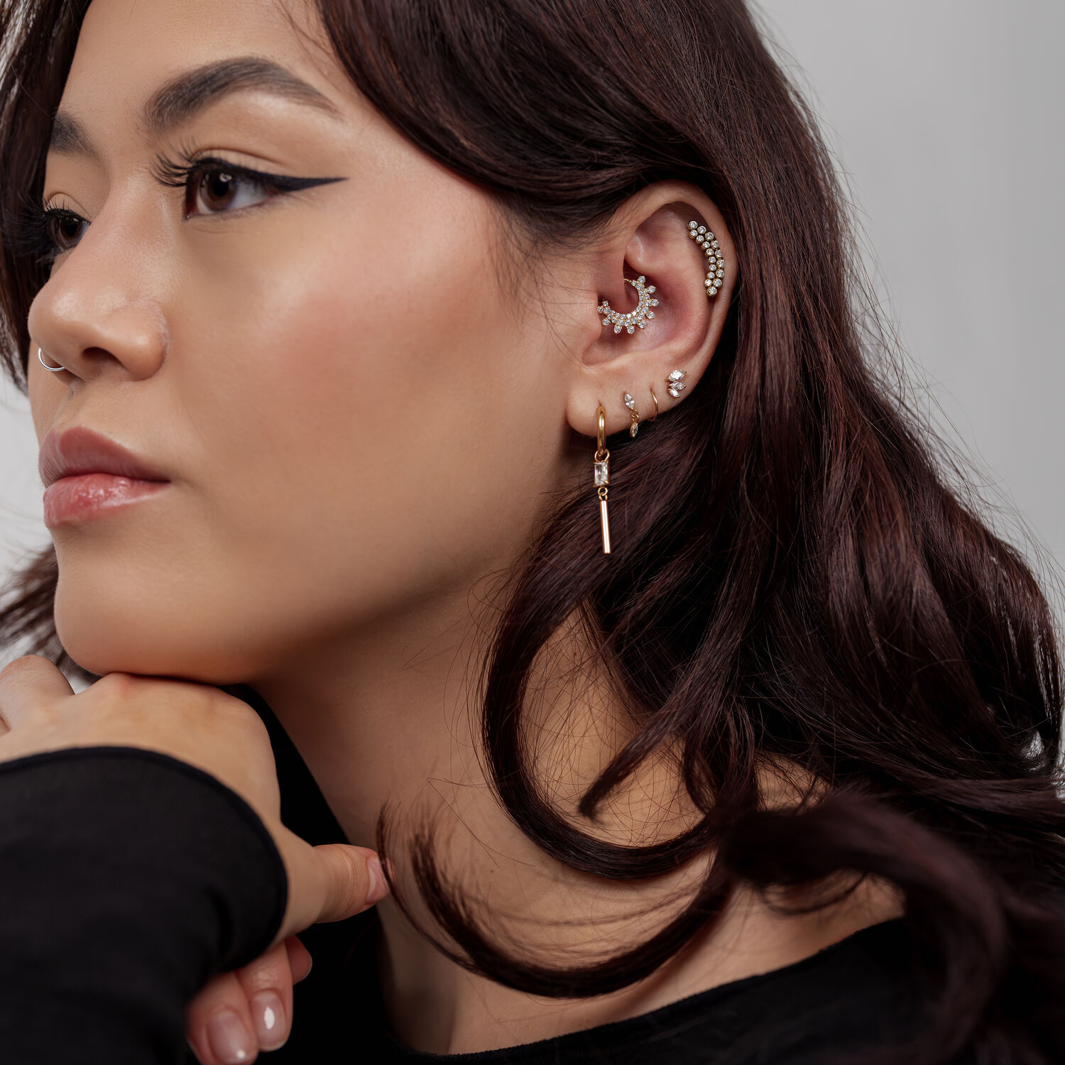 Donna con diversi piercing d'oro alle orecchie e un clicker per setto nasale dorato su sfondo grigio