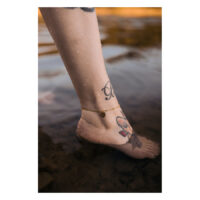 Cavigliera dorata con ciondolo Monstera su caviglia tatuata in acqua