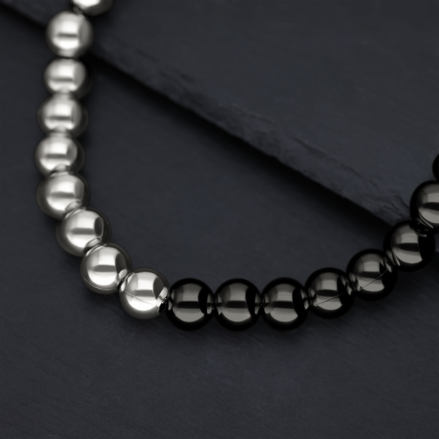 Primo piano di una collana lucente con sfere argento e nere su sfondo scuro