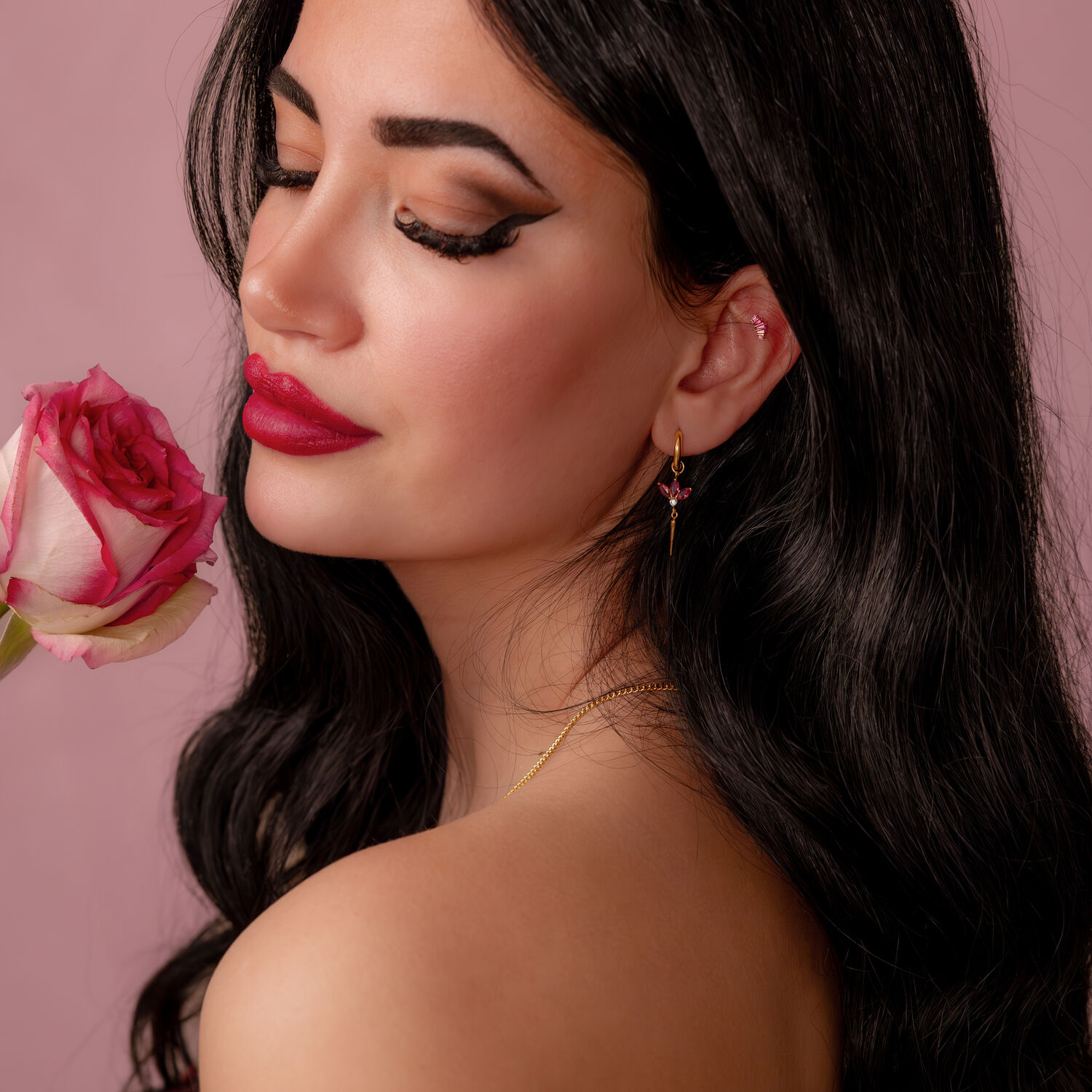 Donna con lunghi capelli neri tiene una rosa, indossa un orecchino dorato