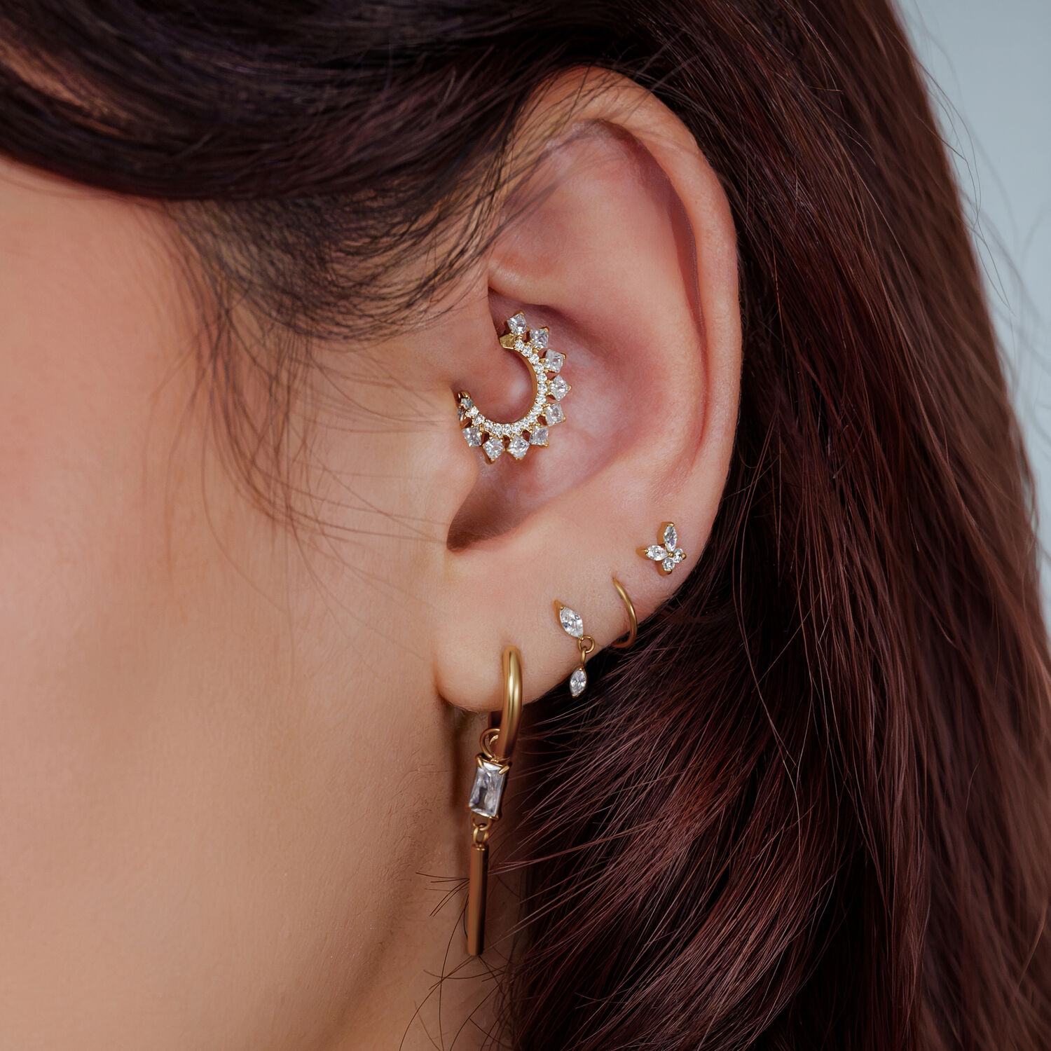 Orecchio con più piercing dorati e decorati con cristalli, primo piano