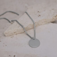 Collana d'argento con ciondolo rotondo su pavimento in pietra chiara