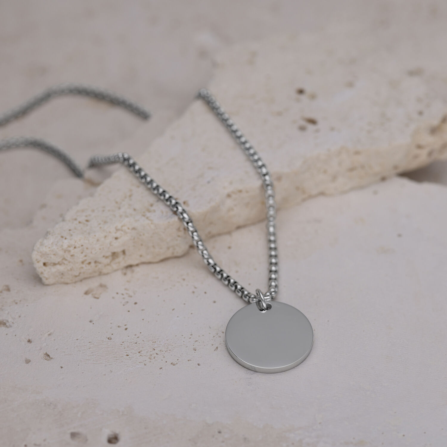 Collana d'argento con ciondolo rotondo su pavimento in pietra chiara