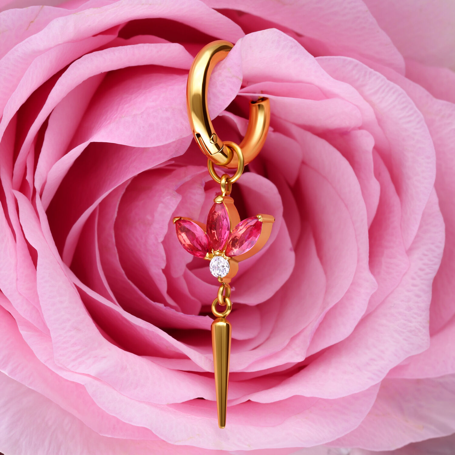 Orecchini dorati con pendente a fiore di cristallo rosa davanti a una rosa