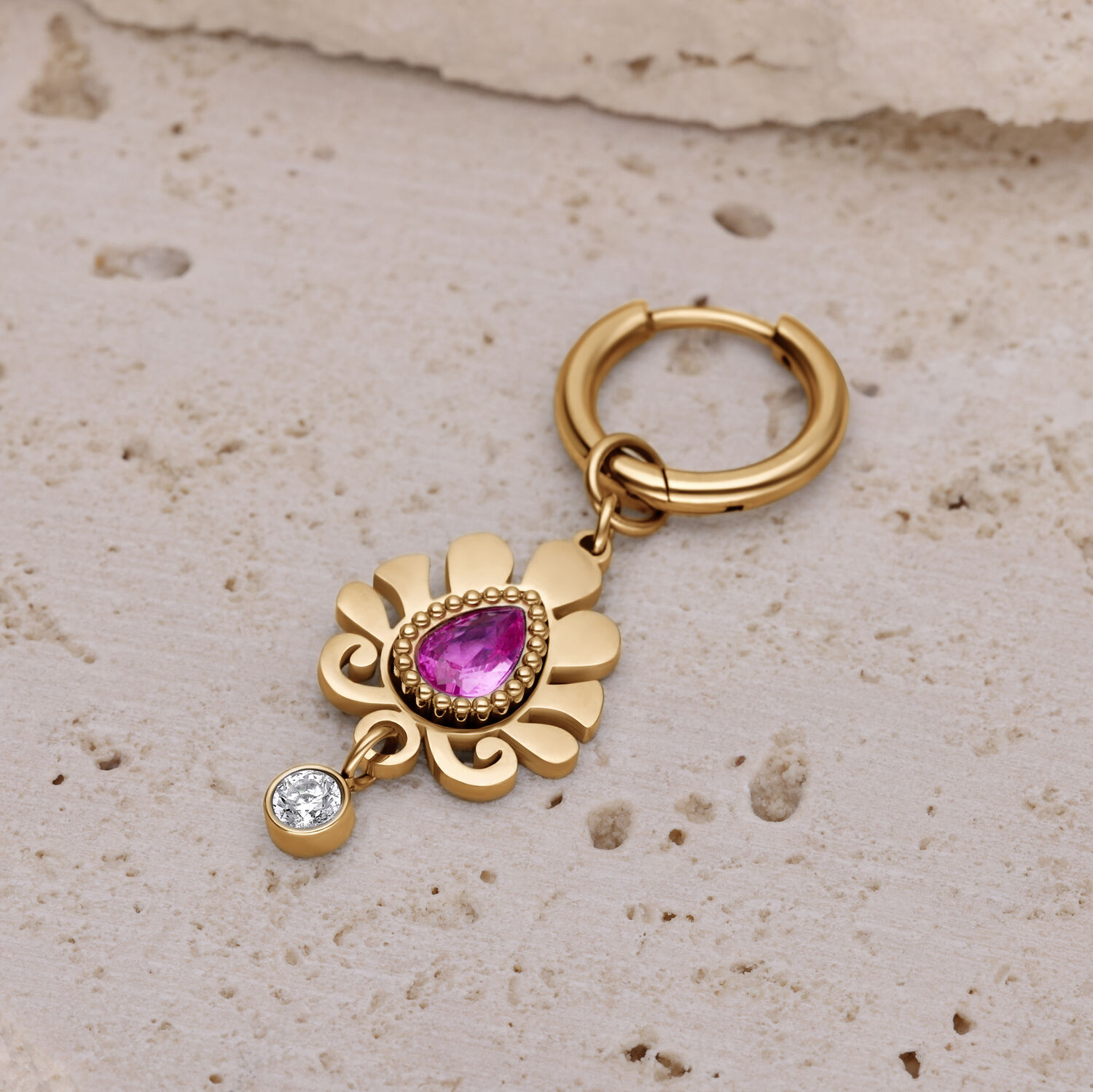 Orecchino dorato con ciondolo di cristallo rosa Orecchino dorato con cristallo rosa a forma di goccia e piccolo ciondolo di cristallo chiaro su superficie di pietra