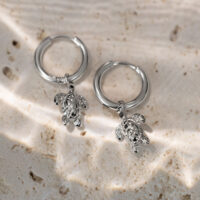 Due creole argentate con piccoli ciondoli a forma di tartaruga su sfondo di pietra chiara