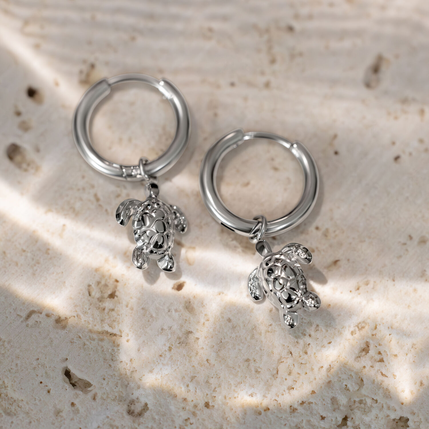 Due creole argentate con piccoli ciondoli a forma di tartaruga su sfondo di pietra chiara