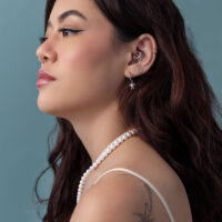 Donna con lunghi capelli castani, orecchini tartaruga argento, collana di perle, sfondo blu