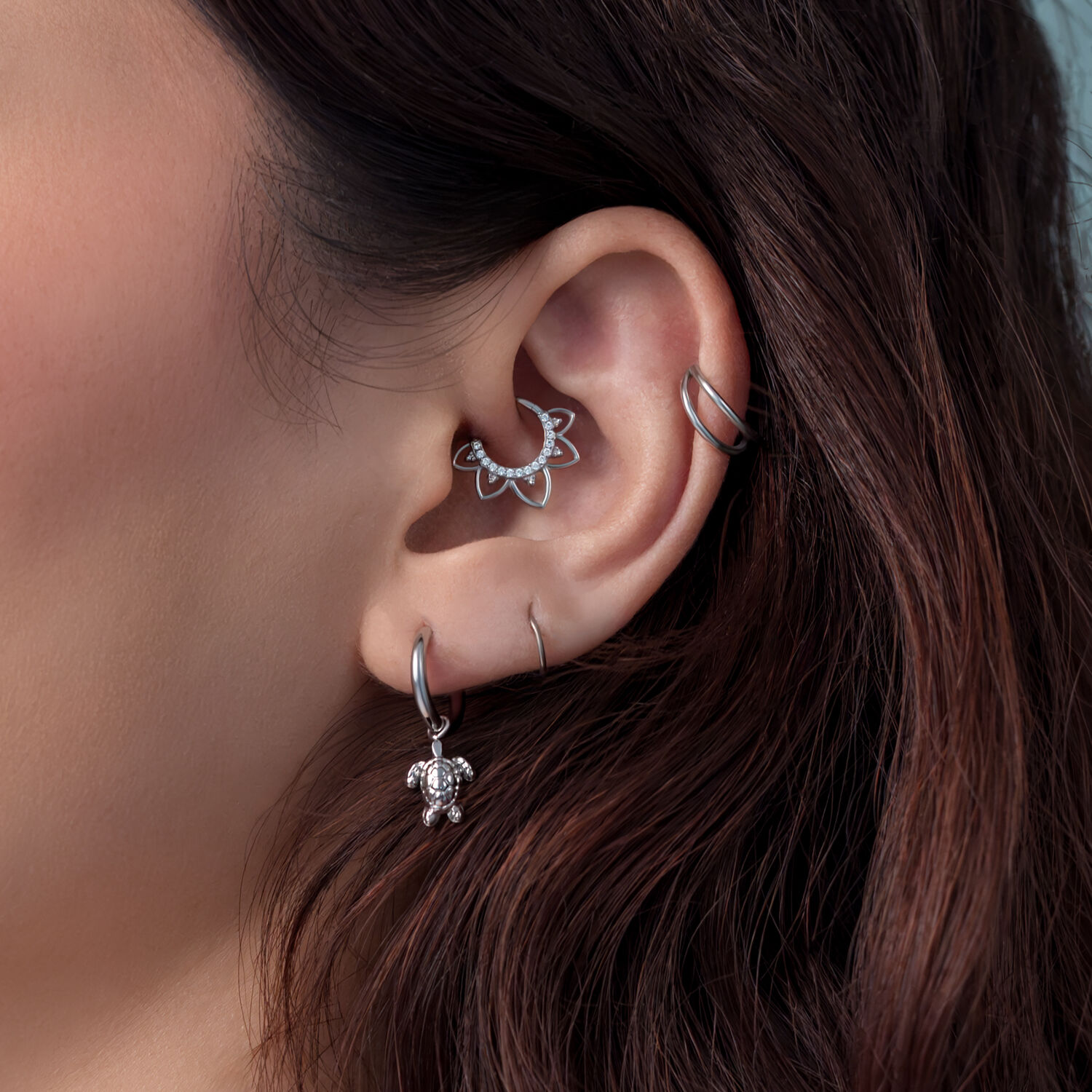 Primo piano di un orecchio con orecchini a tartaruga d'argento e altri piercing, capelli castani sullo sfondo