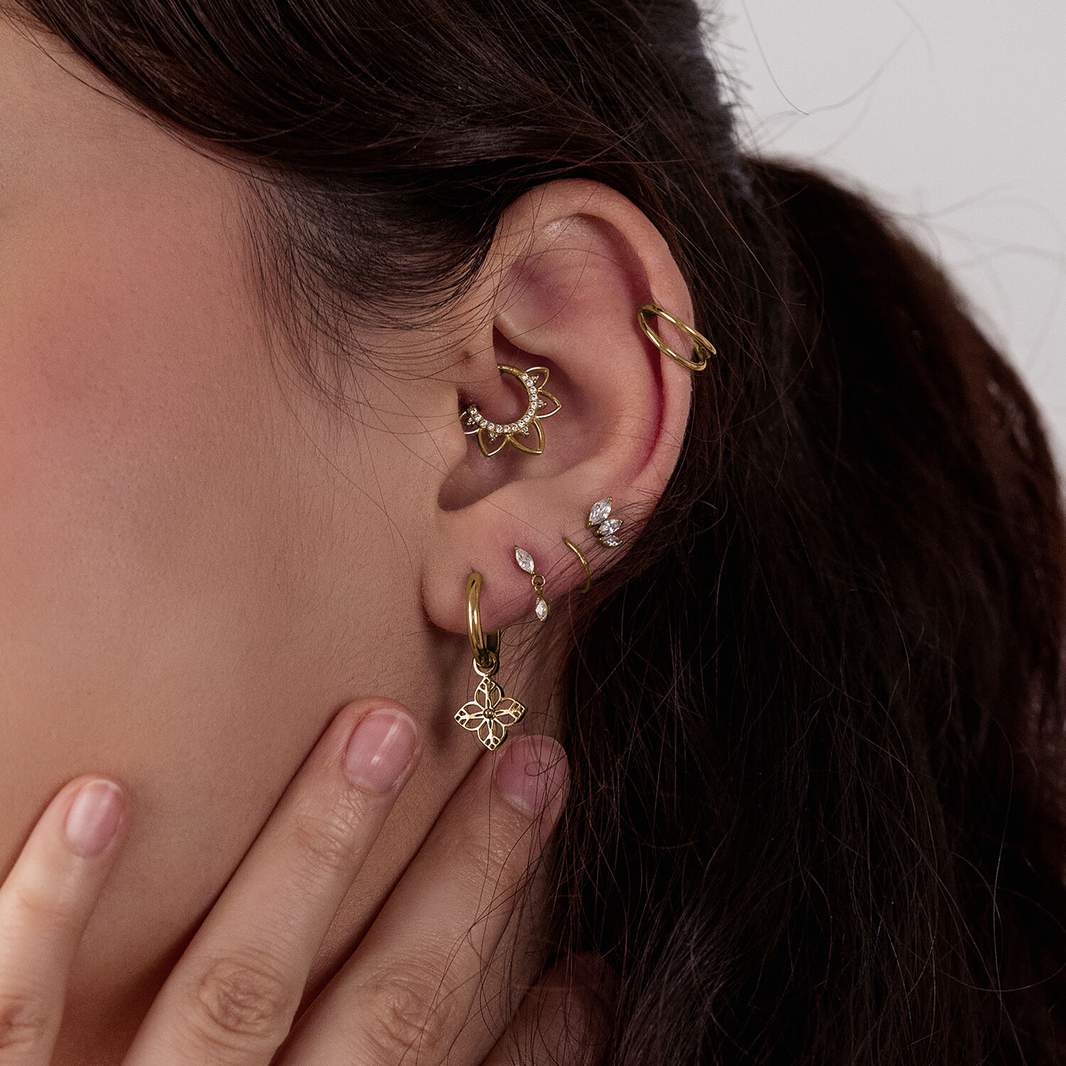 Orecchini dorati con design floreale Orecchini dorati su orecchio con più piercing, primo piano