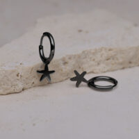 Due orecchini neri con ciondolo a stella marina su superficie di pietra chiara