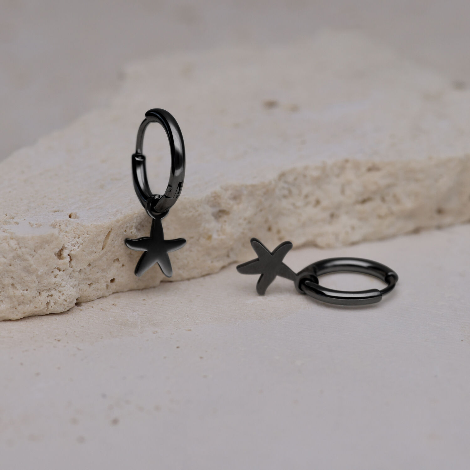 Due orecchini neri con ciondolo a stella marina su superficie di pietra chiara