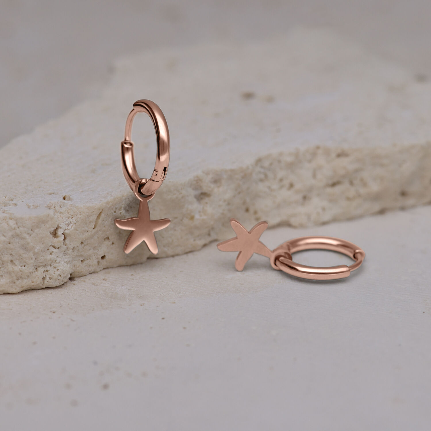 Due orecchini a cerchio in oro rosa con ciondoli a forma di stella marina su pietra chiara