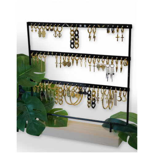 Espositore in metallo nero con orecchini su base in legno, circondato da foglie verdi