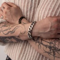 Persona con braccia tatuate indossa un bracciale Chunky argento, braccia incrociate su un maglione color crema