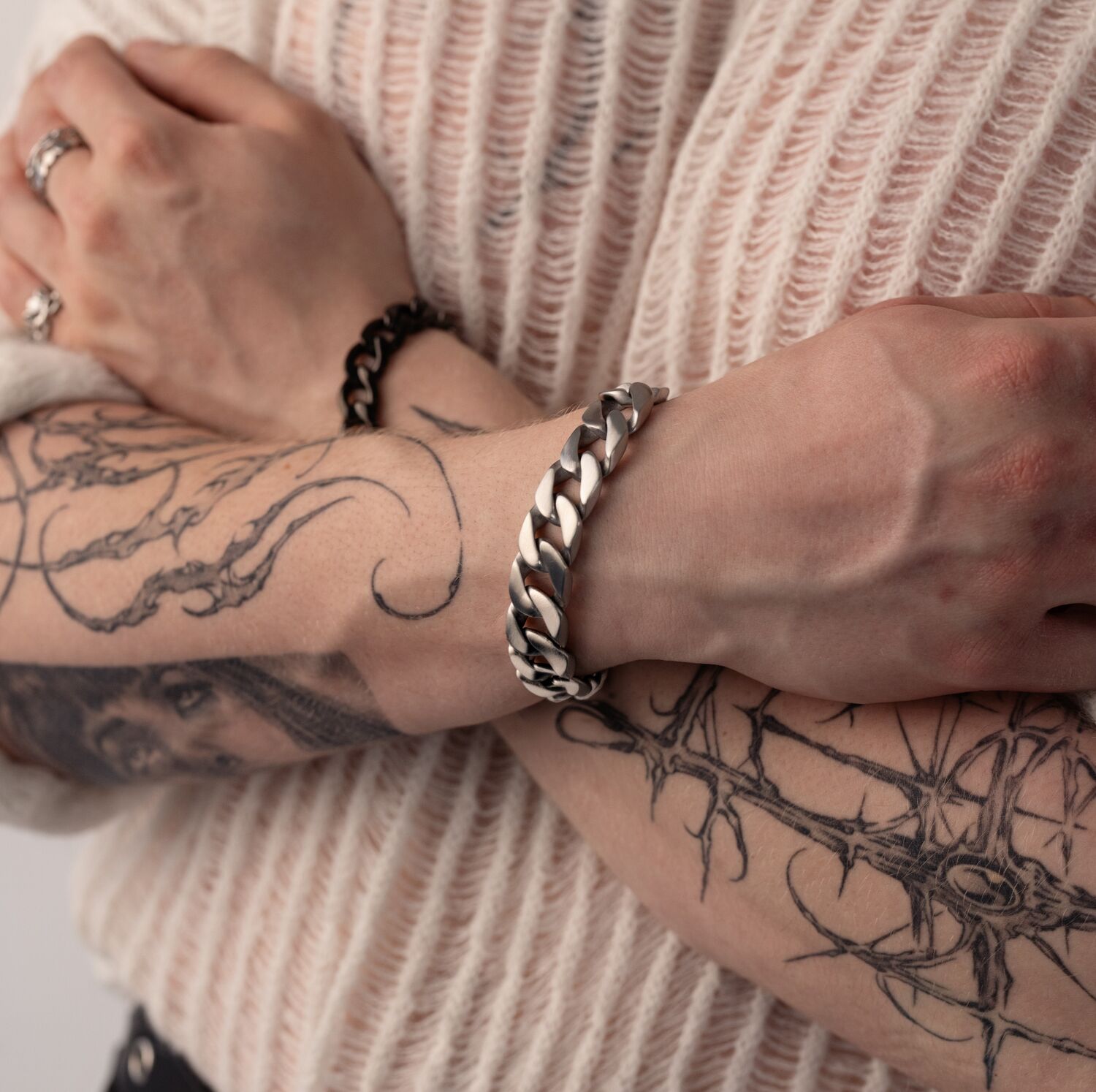 Persona con braccia tatuate indossa un bracciale Chunky argento, braccia incrociate su un maglione color crema