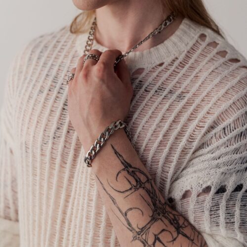 Persona con braccio tatuato indossa un bracciale Chunky in argento e un maglione lavorato a maglia