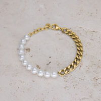 Bracciale con perle sintetiche bianche e catena a maglie dorata su sfondo beige