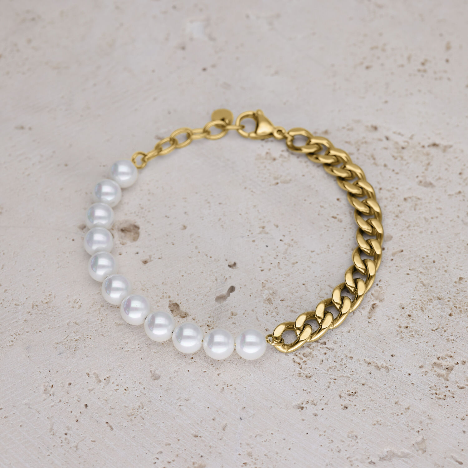 Bracciale con perle sintetiche bianche e catena a maglie dorata su sfondo beige