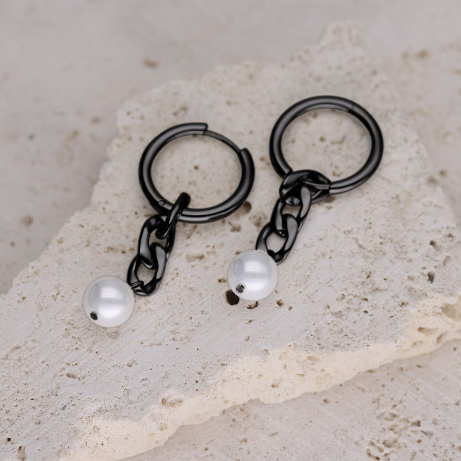 Due orecchini a cerchio neri con maglie a catena e perle bianche su pietra chiara