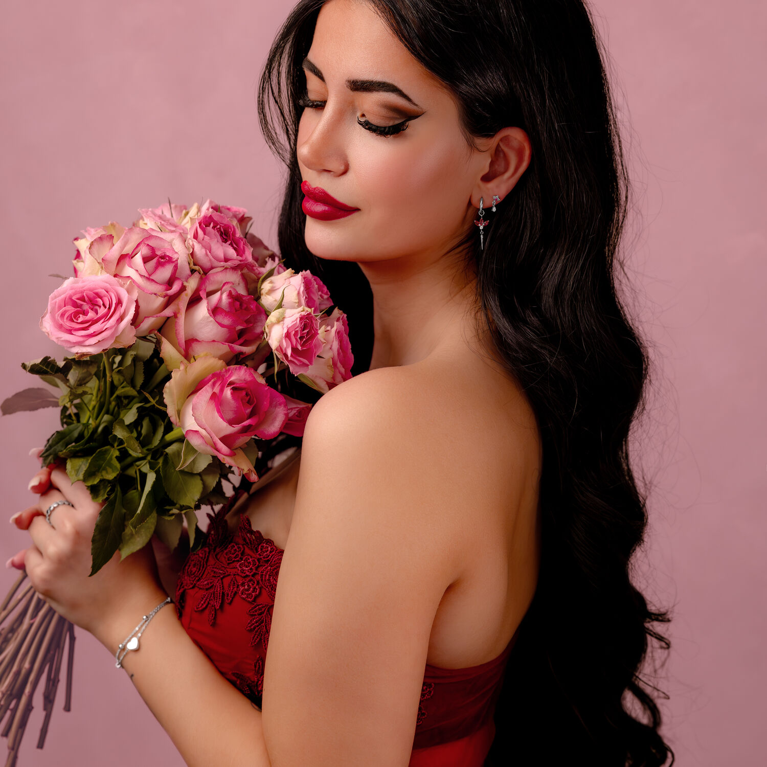 Donna con lunghi capelli scuri tiene un mazzo di rose rosa su sfondo rosa.