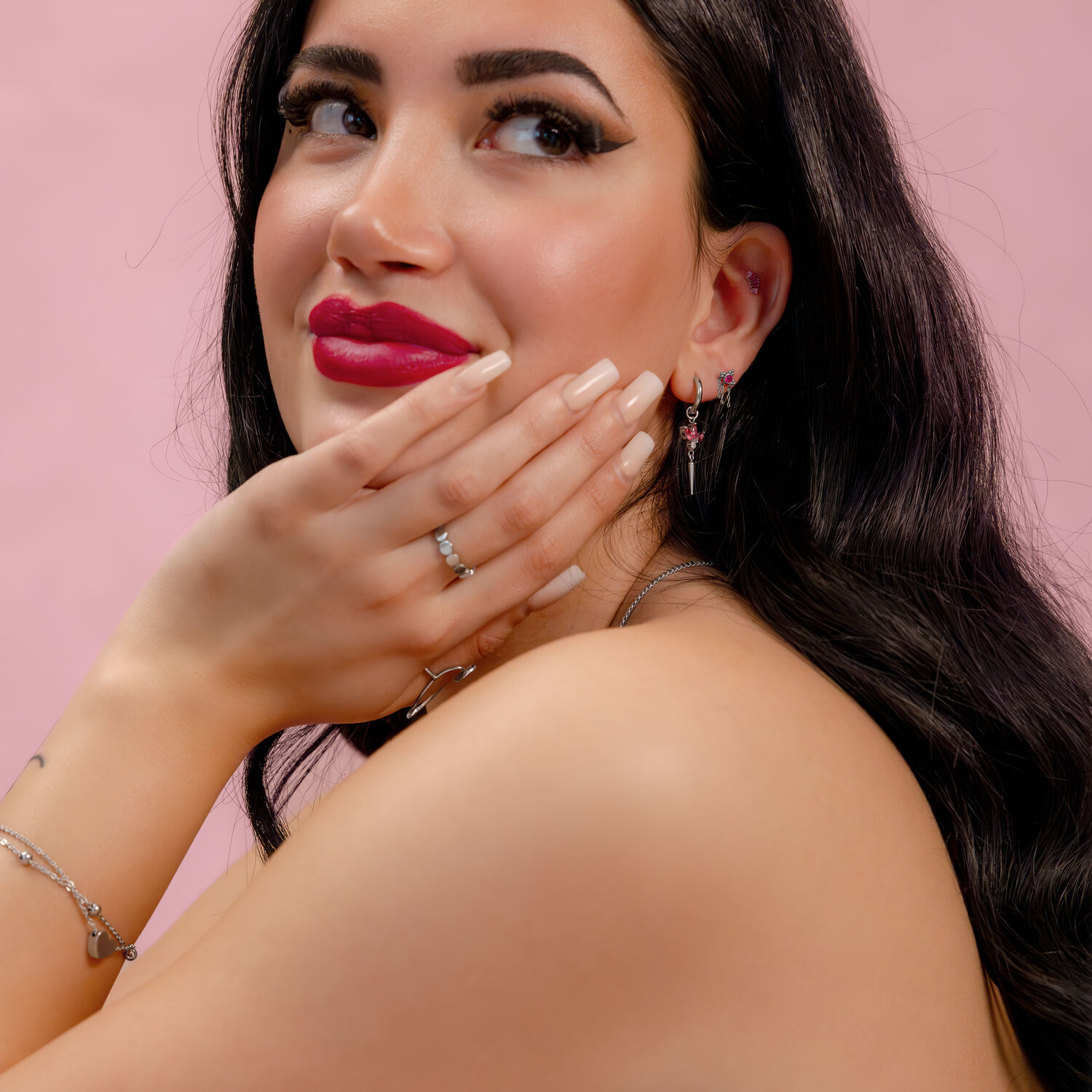 Donna con lunghi capelli scuri che indossa gioielli d'argento con cristalli rossi su sfondo rosa