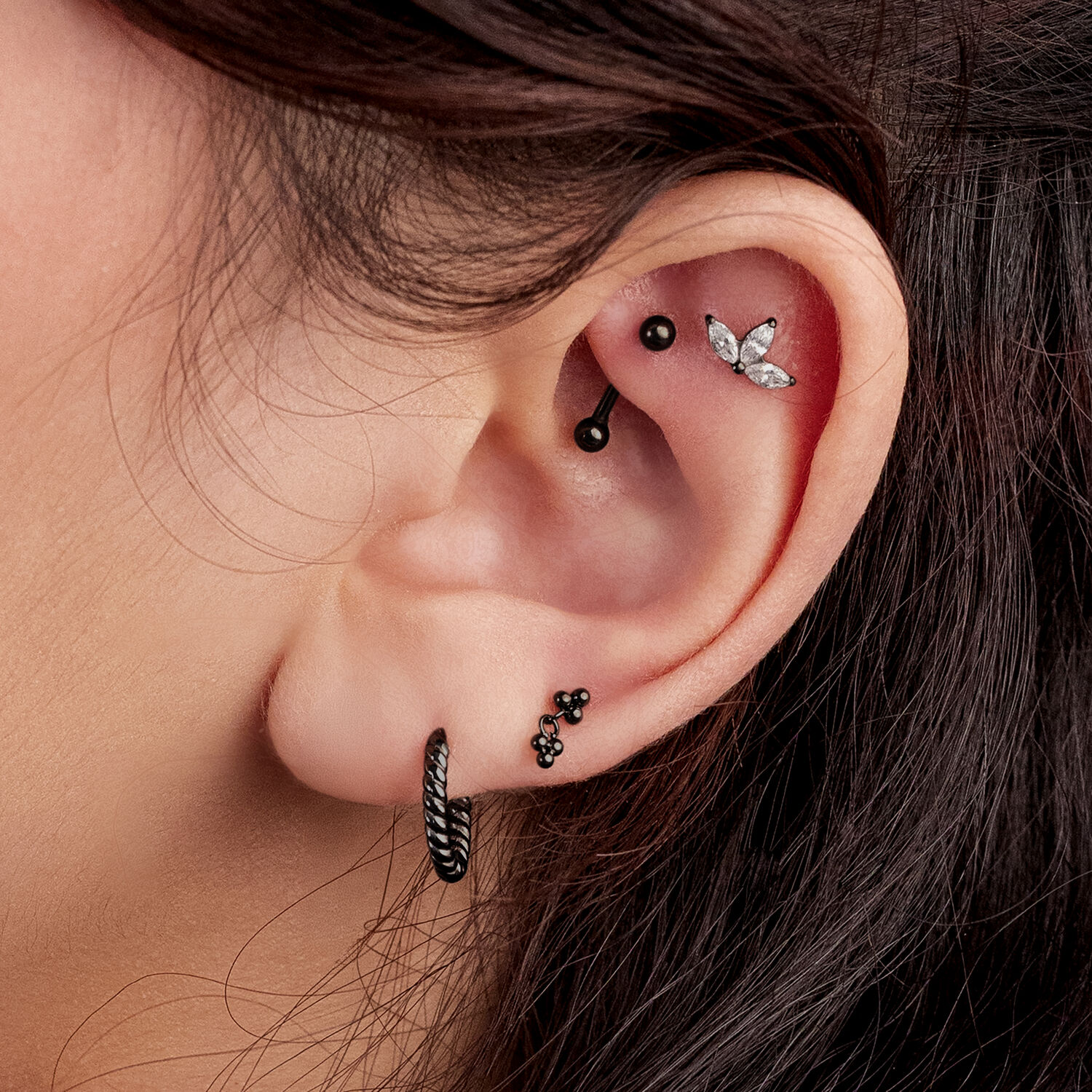 Primo piano di un orecchio con diversi piercing neri, incluso un triplo accessorio.