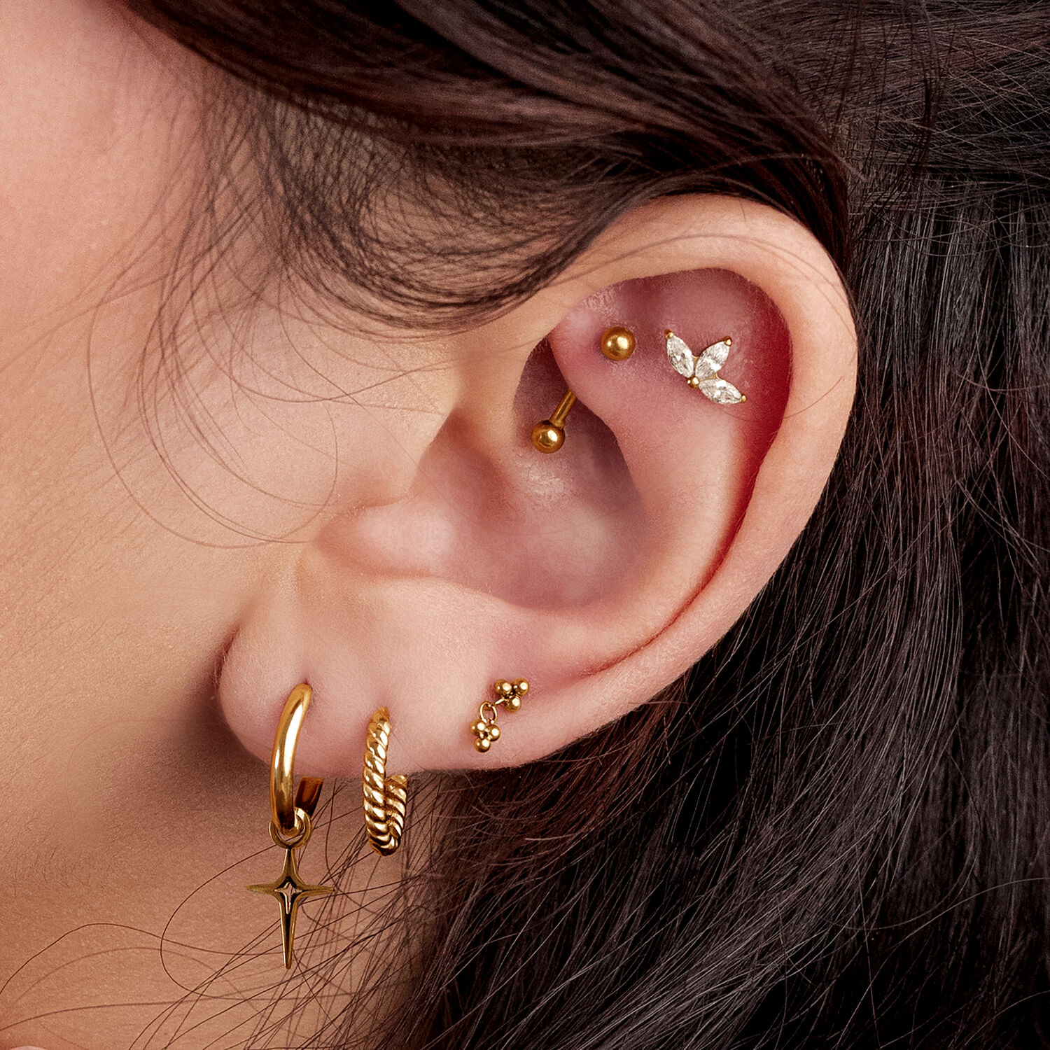 Orecchio con diversi piercing dorati, incluso un accessorio scintillante a tre foglie