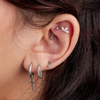 Primo piano di un orecchio con diversi piercing, tra cui un attacco pendente in titanio e altri gioielli d'argento.