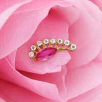 Accessorio dorato con cristallo rosso ovale e pietre chiare su petali rosa