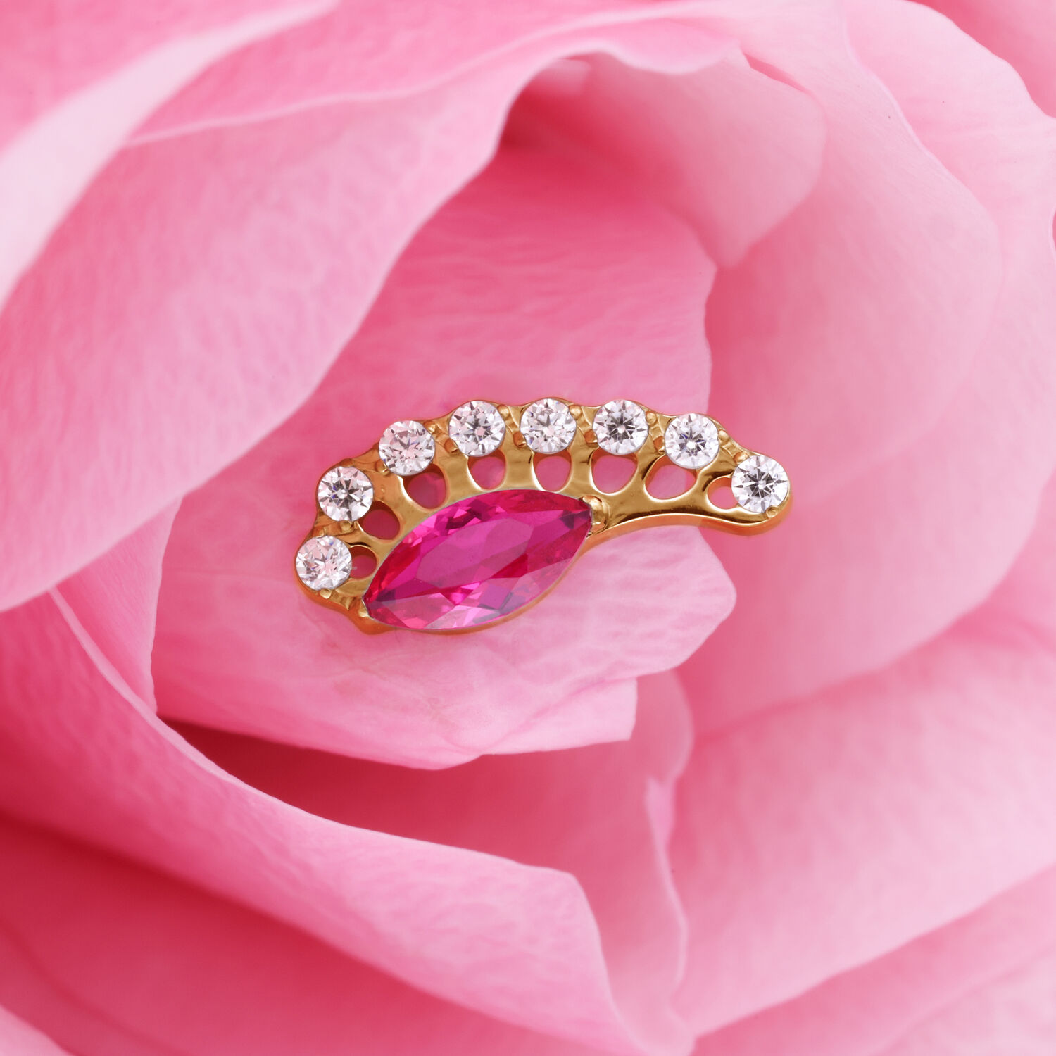 Accessorio dorato con cristallo rosso ovale e pietre chiare su petali rosa