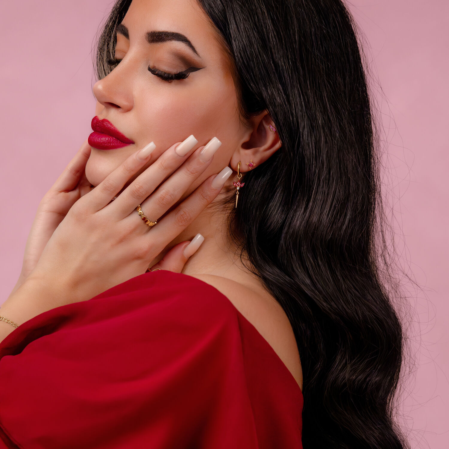 Donna con lunghi capelli neri, labbra rosse e gioielli dorati su sfondo rosa