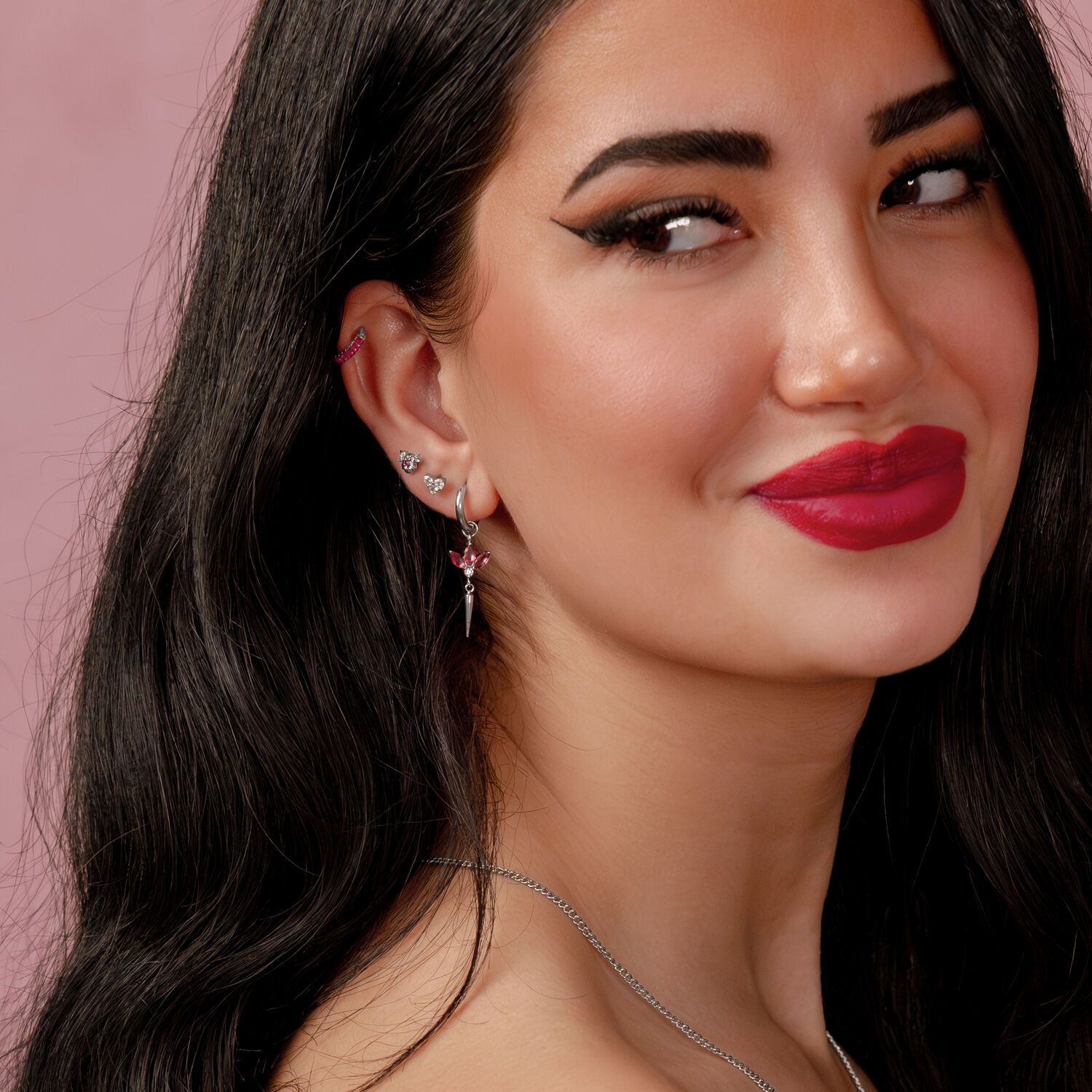 Donna con lunghi capelli neri e orecchino d'argento con rubino rosso su sfondo rosa