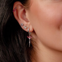 Primo piano di un orecchio con diversi orecchini d'argento e cristalli rossi, capelli scuri sullo sfondo